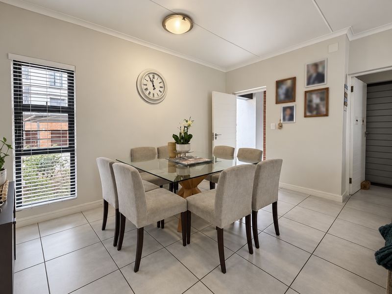 A bright and well-maintained dining area featuring neutral tiled flooring, large windows with venetian blinds, and clean, modern finishes.