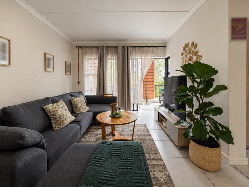 A well-maintained living room featuring neutral tiled flooring, cove cornicing, and direct access to an outdoor balcony through sliding glass doors.