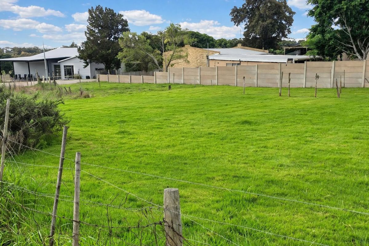 A clear, level residential vacant land plot featuring a well-maintained grass lawn, enclosed by precast concrete boundary walls and wire fencing.