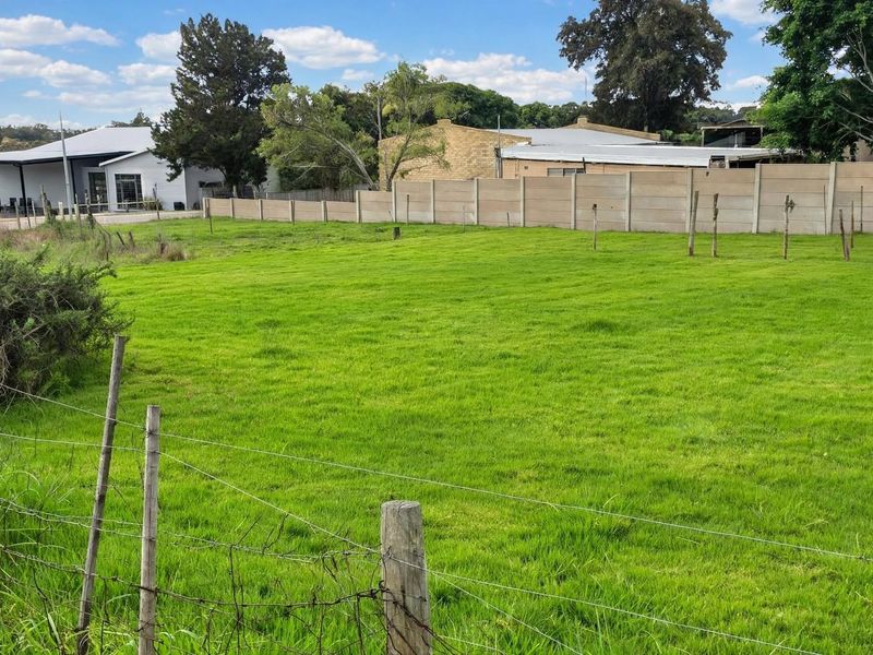 A clear, level residential vacant land plot featuring a well-maintained grass lawn, enclosed by precast concrete boundary walls and wire fencing.