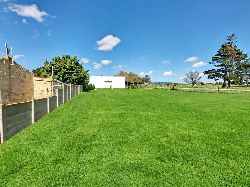 A spacious, well-maintained residential lawn area bordered by a concrete panel wall and stone retaining wall with electric fencing.