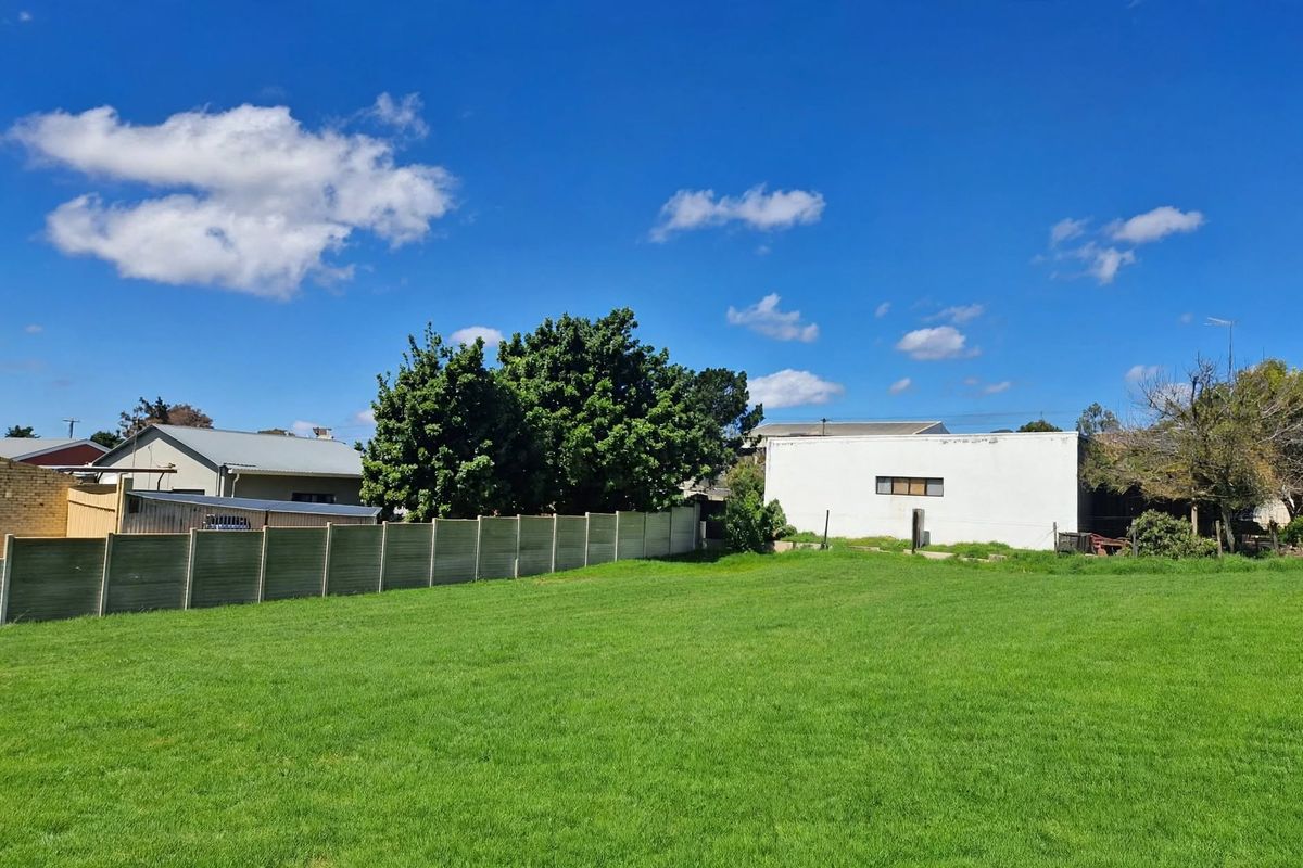 A spacious, well-maintained residential lawn area enclosed by a precast concrete boundary wall, offering a clear view of neighboring properties.