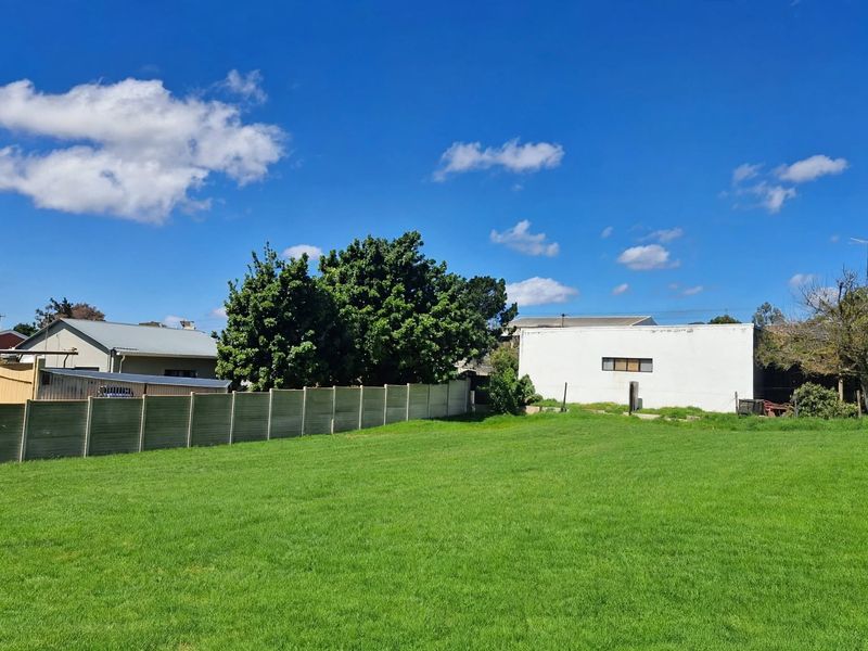 A spacious, well-maintained residential lawn area enclosed by a precast concrete boundary wall, offering a clear view of neighboring properties.