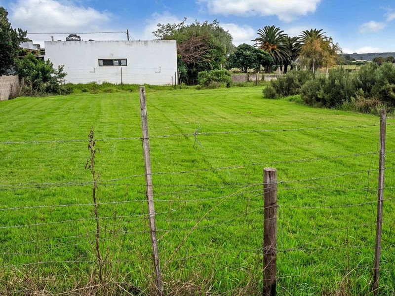 A vacant residential plot featuring a mowed grass lawn, enclosed by a simple barbed wire and wooden post fence.