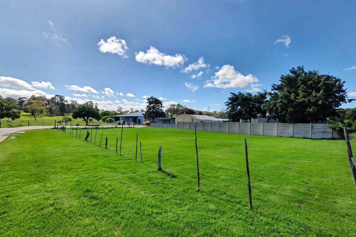 A wide-angle view of a vacant residential plot featuring a well-maintained grass lawn, enclosed by wire fencing and a precast concrete boundary wall.