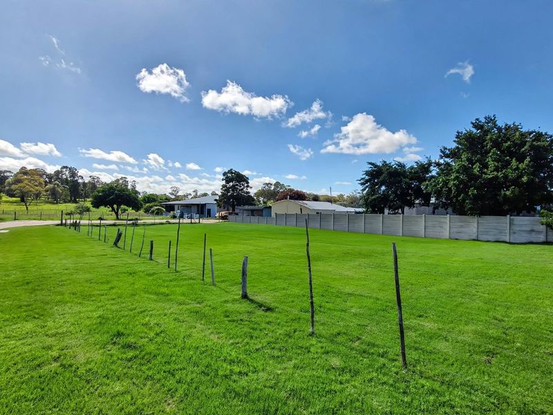 A wide-angle view of a vacant residential plot featuring a well-maintained grass lawn, enclosed by wire fencing and a precast concrete boundary wall.
