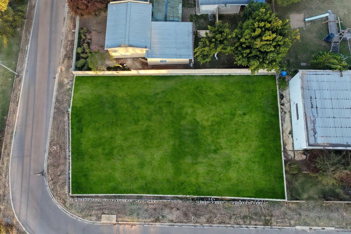 An aerial view of a vacant residential plot featuring a well-maintained grass lawn and perimeter walling, situated in a established neighborhood.