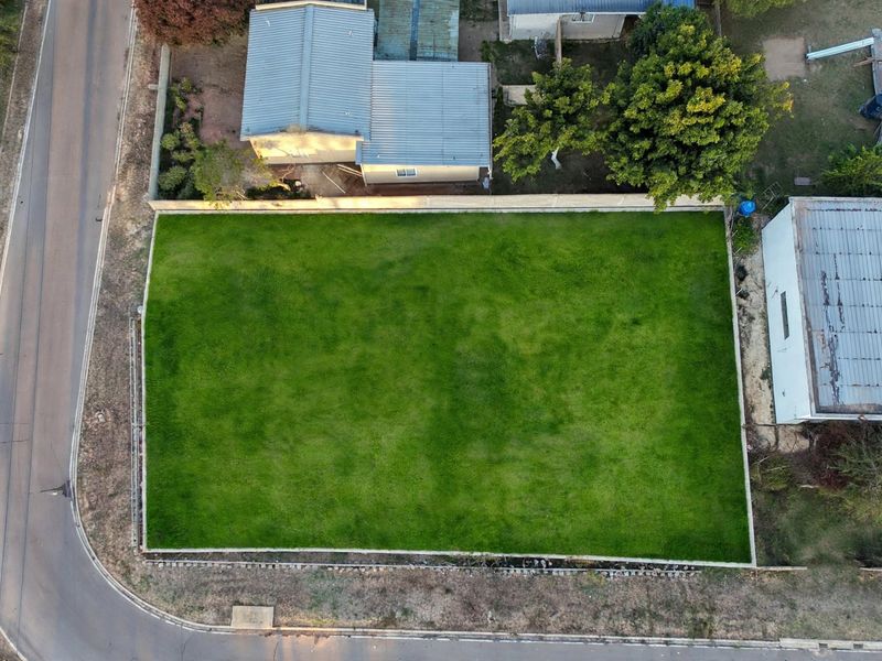 An aerial view of a vacant residential plot featuring a well-maintained grass lawn and perimeter walling, situated in a established neighborhood.