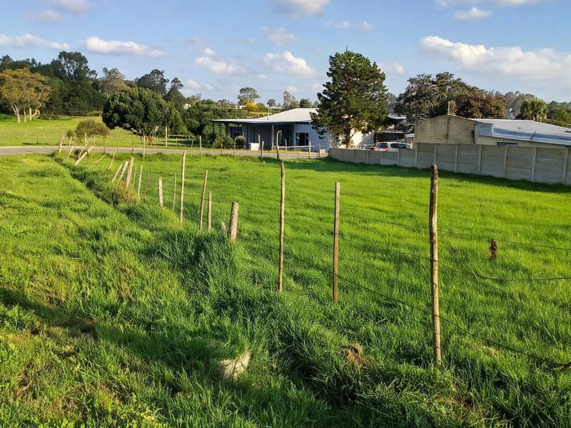 A vacant residential plot featuring grassy terrain, enclosed by wire fencing and wooden posts, with a precast concrete boundary wall in the background.
