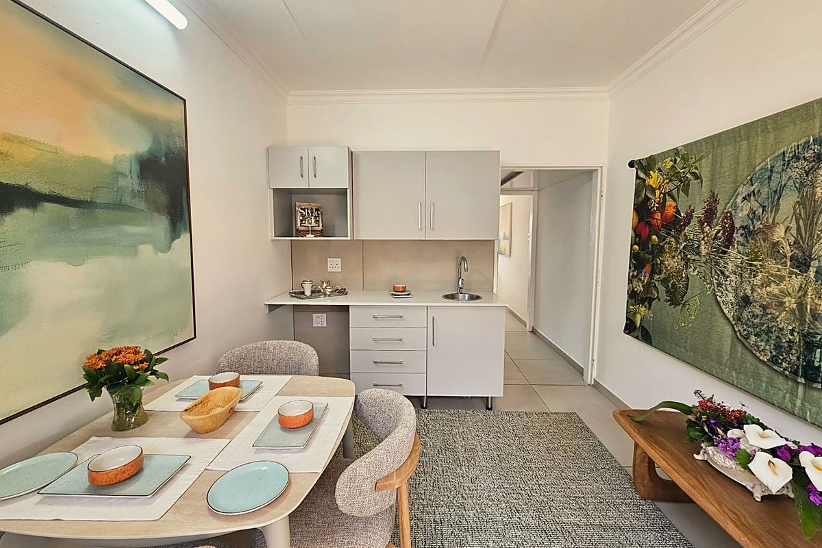 A compact kitchenette featuring modern grey cabinetry, a stainless steel sink, and neutral countertops, integrated into a functional living and dining space.