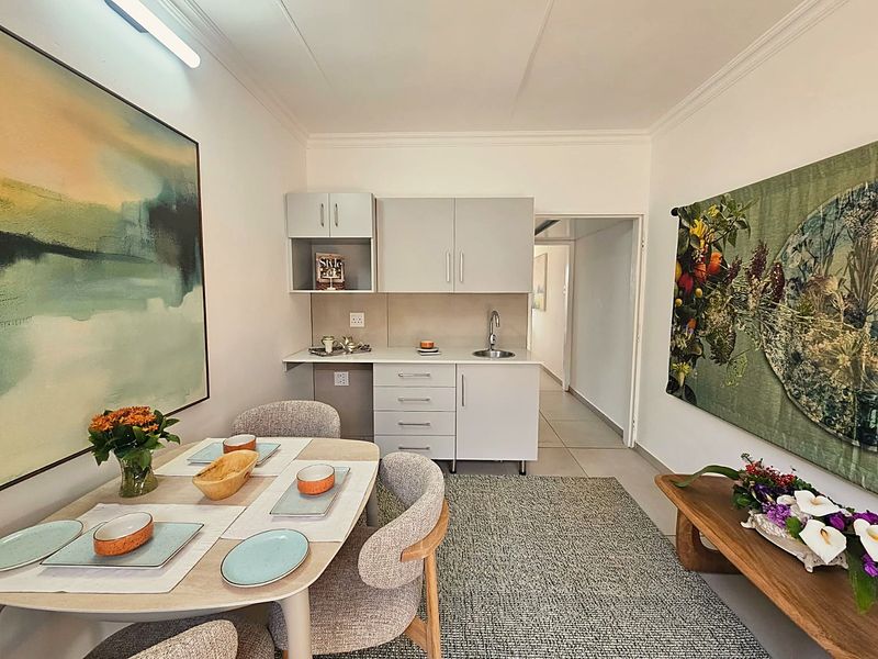 A compact kitchenette featuring modern grey cabinetry, a stainless steel sink, and neutral countertops, integrated into a functional living and dining space.