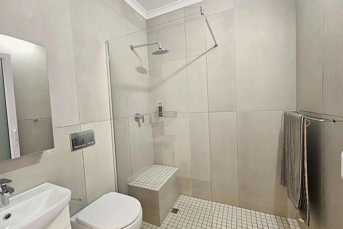 Modern bathroom featuring a walk-in shower with a built-in bench, rain shower head, wall-hung toilet with concealed cistern, and contemporary large format tiling.