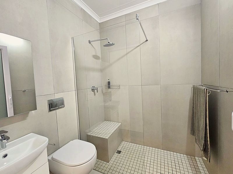 Modern bathroom featuring a walk-in shower with a built-in bench, rain shower head, wall-hung toilet with concealed cistern, and contemporary large format tiling.