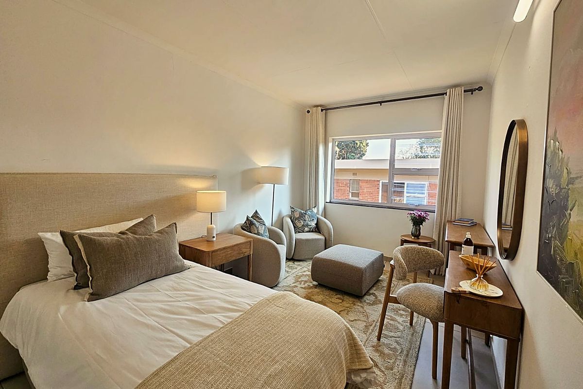 A well-maintained bedroom featuring neutral tones, a large window providing natural light, and a functional layout suitable for comfortable retirement living.