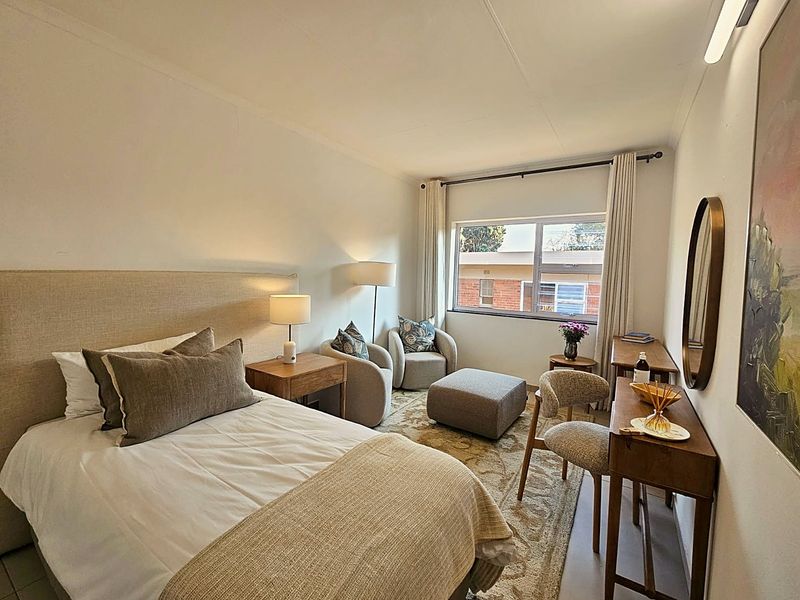 A well-maintained bedroom featuring neutral tones, a large window providing natural light, and a functional layout suitable for comfortable retirement living.