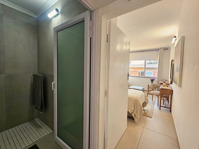 A modern bathroom featuring a walk-in shower with a frosted glass door, adjacent to a bedroom area with neutral tiled flooring.
