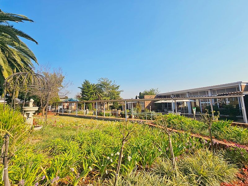 A well-maintained retirement village garden featuring a long covered walkway, landscaped flower beds, and a decorative fountain in a peaceful outdoor setting.