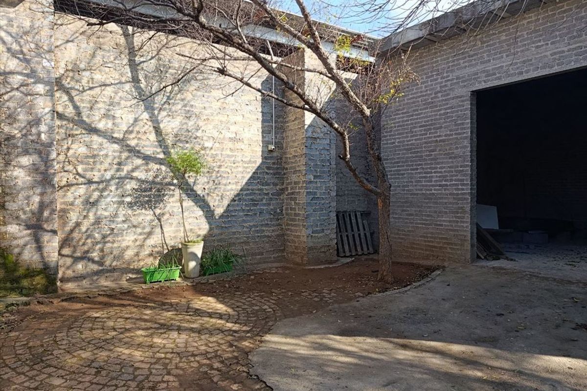 A rustic outdoor courtyard area featuring exposed brick walls, a combination of cobblestone and concrete paving, and a mature tree.