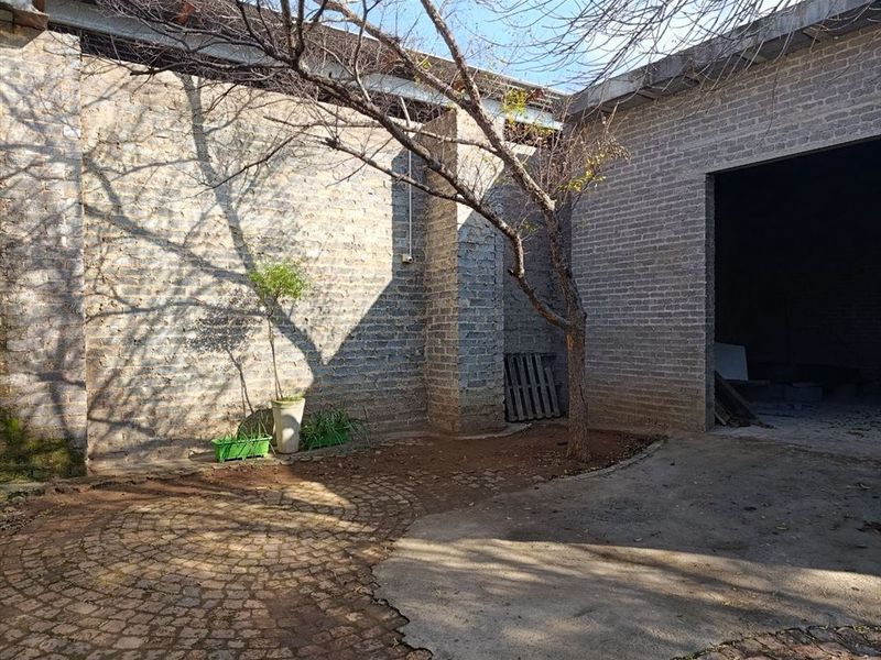 A rustic outdoor courtyard area featuring exposed brick walls, a combination of cobblestone and concrete paving, and a mature tree.