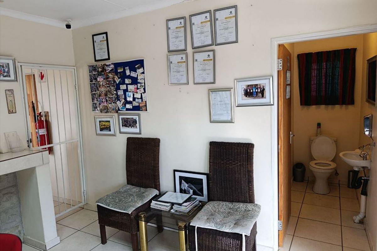 A functional utility or waiting area featuring tiled flooring, a security gate, and an adjacent small bathroom with a toilet and basin.