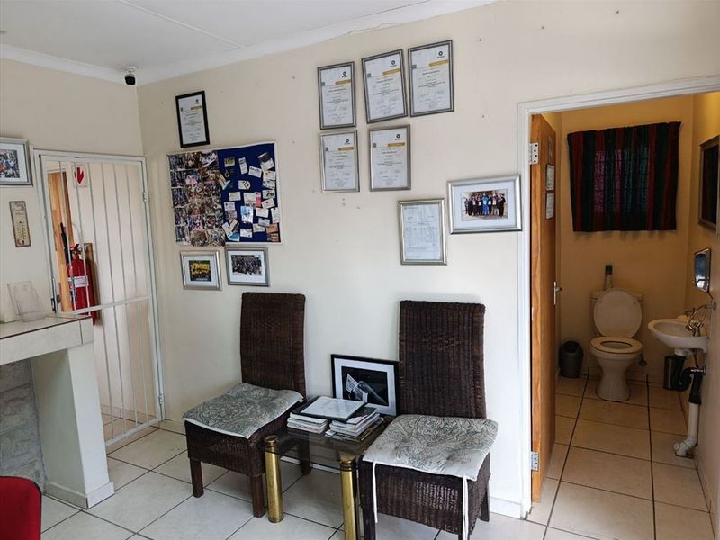 A functional utility or waiting area featuring tiled flooring, a security gate, and an adjacent small bathroom with a toilet and basin.