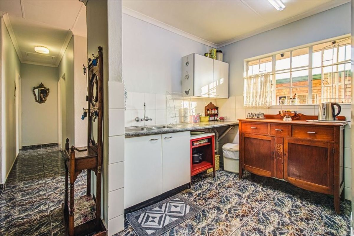 A compact kitchen area featuring tiled flooring, wall-mounted cabinetry, and a sink with a tiled splashback, adjacent to a hallway.