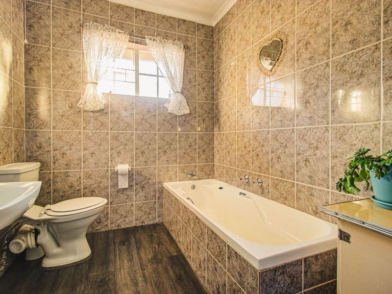 A functional bathroom featuring a built-in bathtub, pedestal basin, and toilet, finished with full-height wall tiling and dark wood-look flooring.