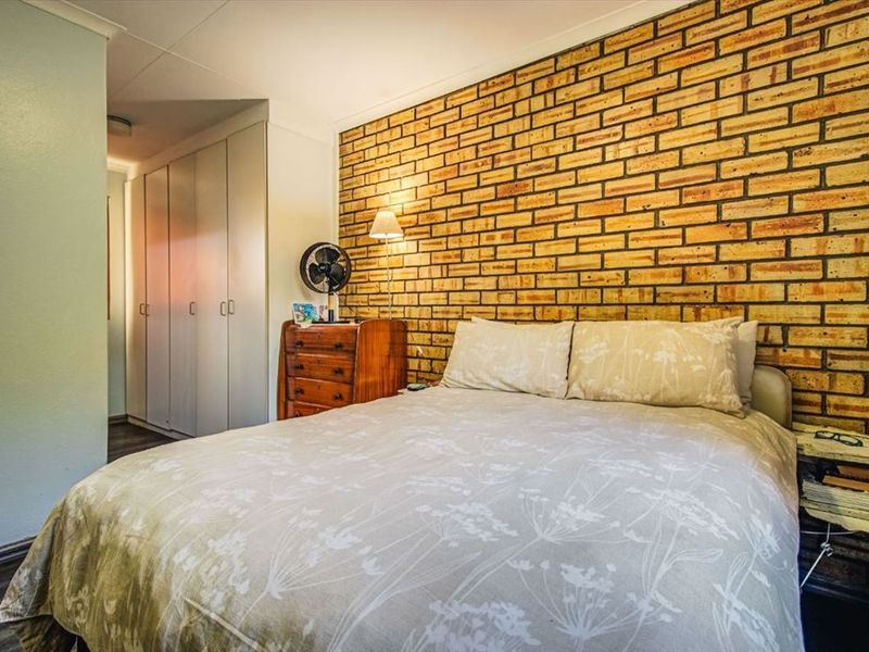 A bedroom featuring an exposed brick feature wall, built-in cupboards, and laminate flooring.