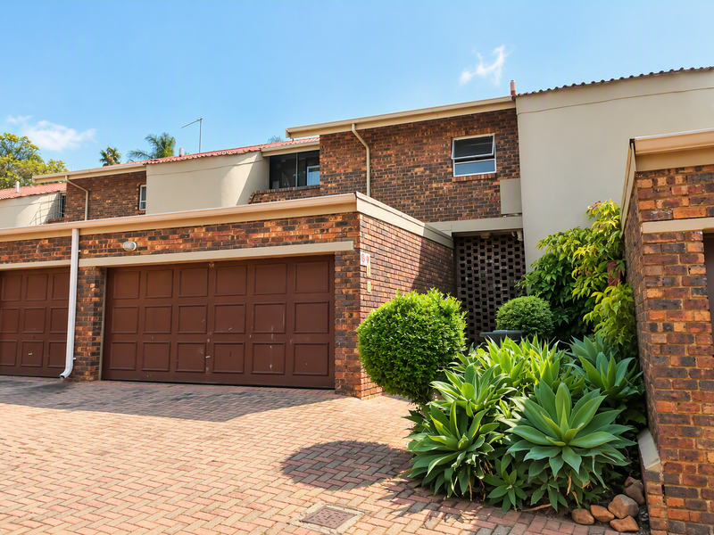 Front elevation of a brick apartment complex featuring a paved driveway and double garage access.