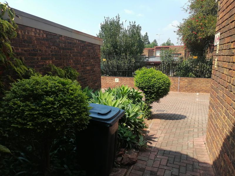 A paved rear courtyard area featuring established garden shrubs and enclosed by brick boundary walls with security fencing.