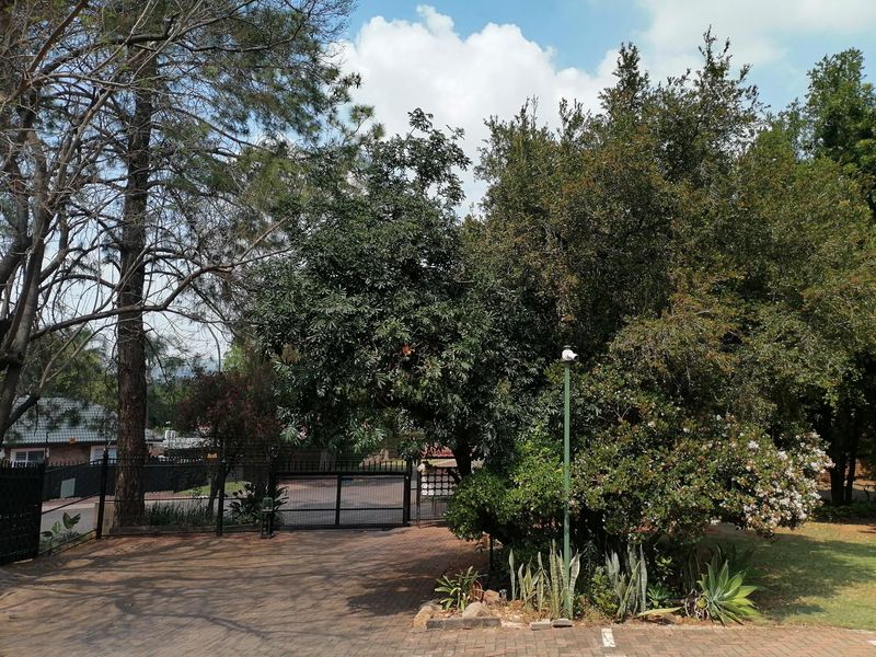 A view of the property entrance featuring a paved driveway, secure perimeter fencing, and a gated access point surrounded by mature trees.