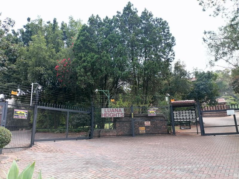 The entrance to Luana Heights apartment complex featuring secure gated access, electric fencing, and brick paved driveway.