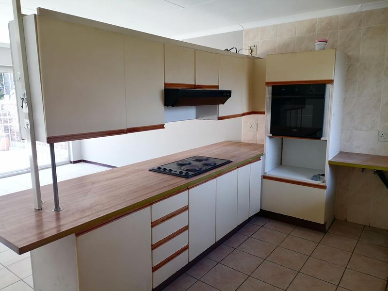 A dated kitchen featuring built-in cabinetry, a laminate countertop, an integrated oven, and an electric hob, with tiled flooring and backsplash throughout.