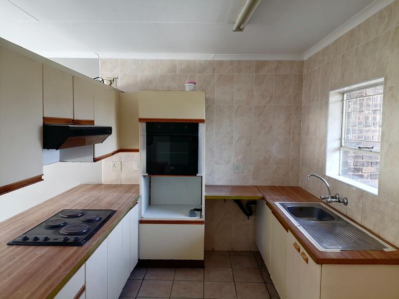 A dated kitchen featuring built-in cabinetry, laminate countertops, an electric hob, oven, and a stainless steel sink with tiled backsplash and flooring.