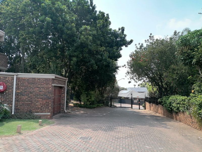 A paved driveway leading to a secure gated entrance with brick boundary walls and a detached brick garage structure.