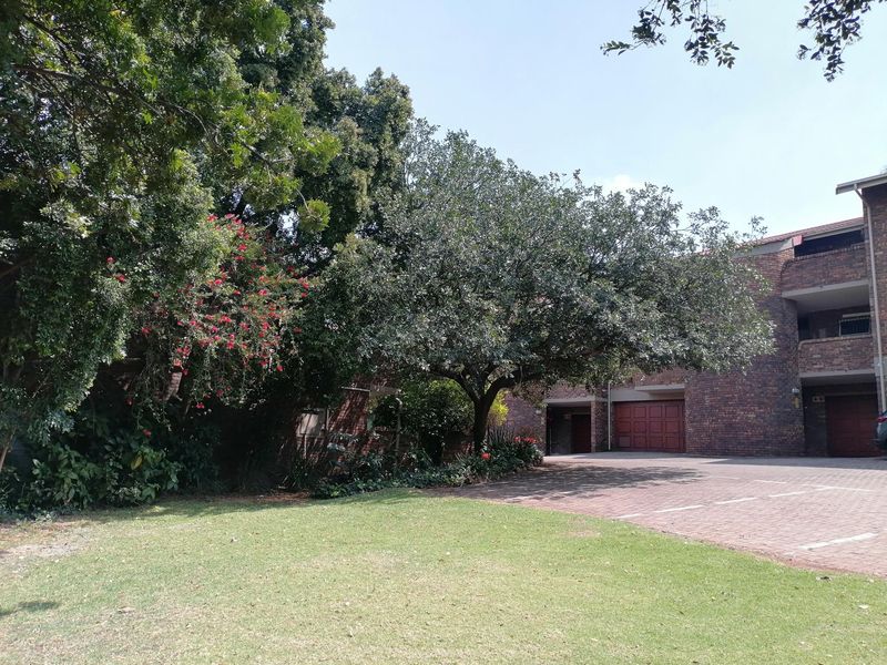 Front view of the apartment complex featuring a face brick facade, paved driveway, integrated garage doors, and established garden landscaping.