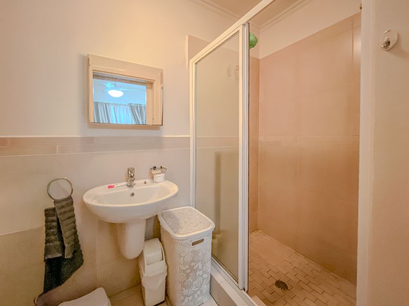 A functional bathroom featuring a pedestal washbasin, a shower enclosure with tiled walls, and a wall-mounted mirror.