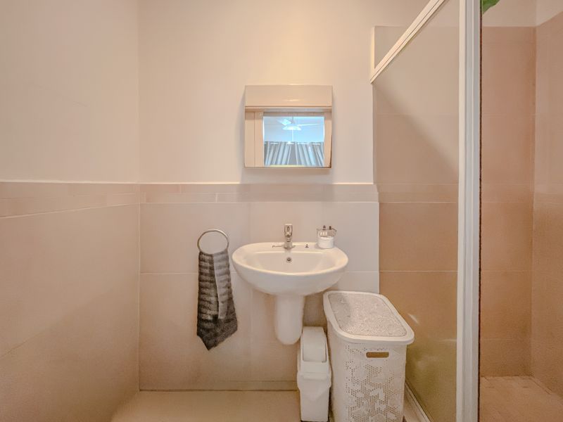 A functional bathroom featuring a pedestal washbasin, wall-mounted mirror cabinet, and a glass-enclosed shower with neutral wall tiling.