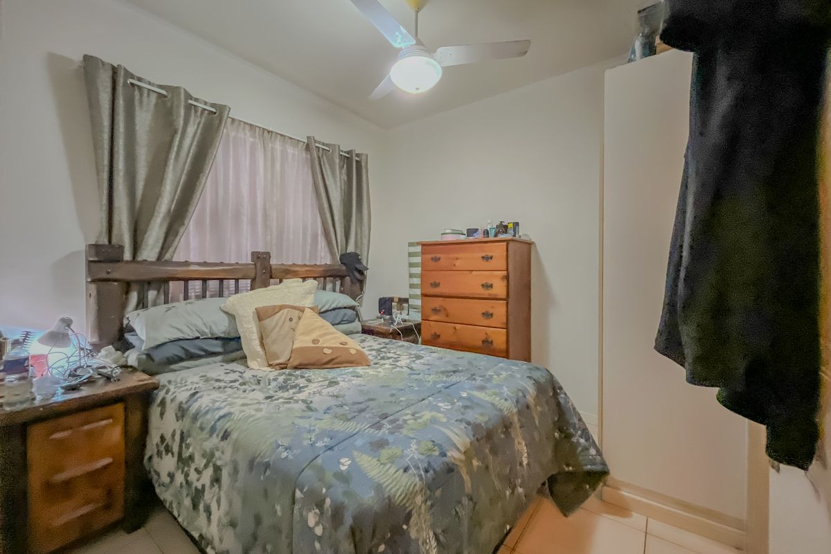 A functional bedroom featuring tiled flooring, a ceiling fan, and a built-in wardrobe, providing essential storage and comfort.