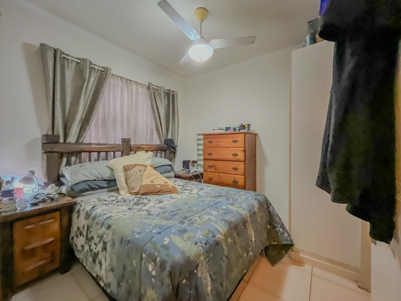 A functional bedroom featuring tiled flooring, a ceiling fan, and a built-in wardrobe, providing essential storage and comfort.