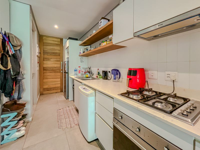 Compact modern kitchen featuring stone countertops, gas hob, built-in oven, extractor fan, and open shelving with clean white cabinetry.