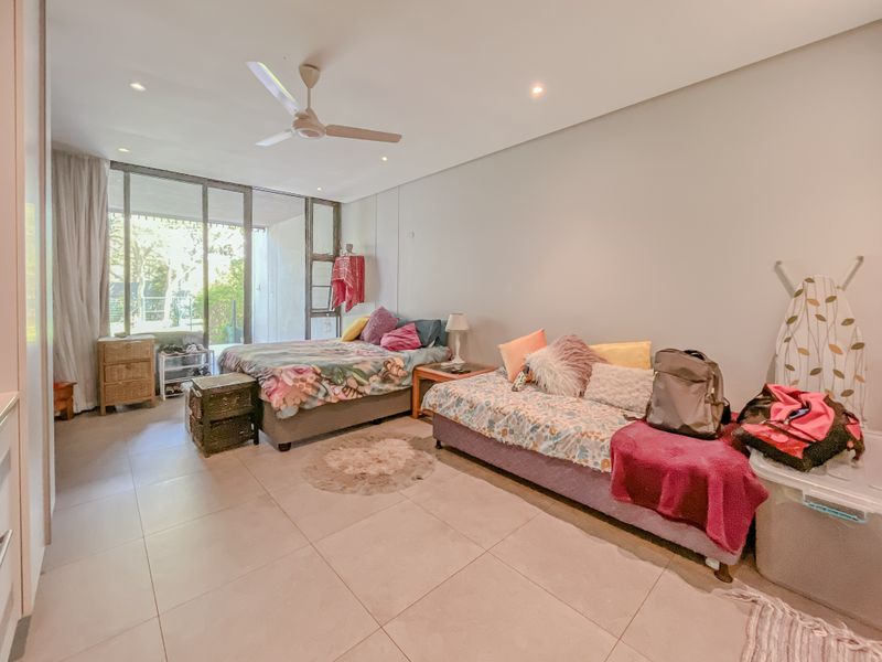 Spacious bedroom featuring large sliding glass doors leading to an outdoor area, neutral tiled flooring, and a ceiling fan.