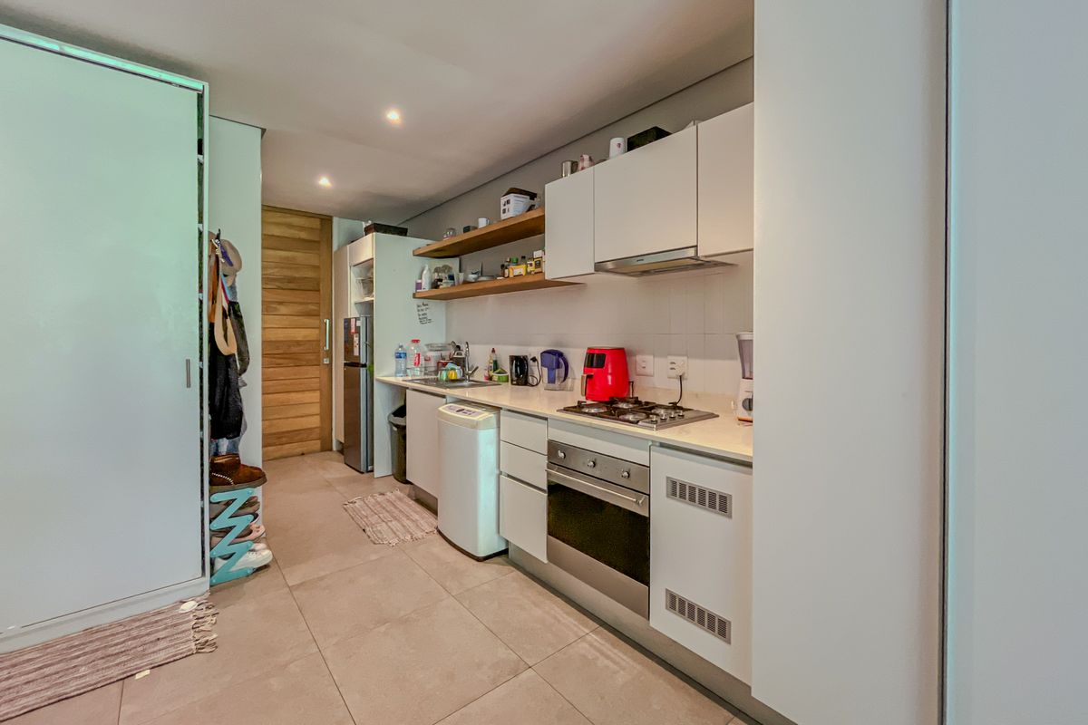 A compact, modern kitchen featuring white cabinetry, stone countertops, a gas hob, an integrated oven, and floating shelving with recessed lighting.