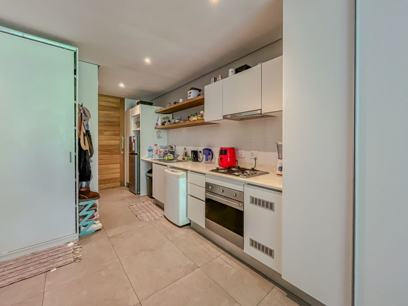 A compact, modern kitchen featuring white cabinetry, stone countertops, a gas hob, an integrated oven, and floating shelving with recessed lighting.