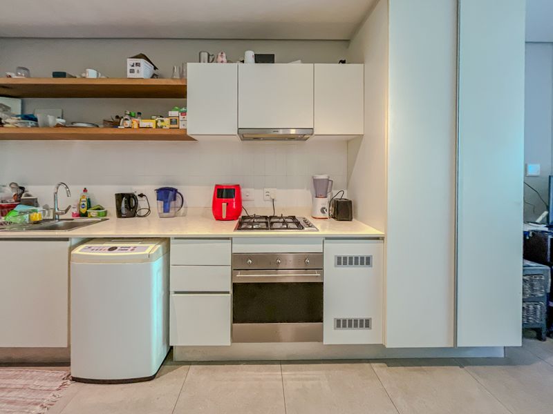 Modern kitchen featuring white cabinetry, built-in oven, gas hob, extractor fan, stainless steel sink, and floating timber shelving with tiled splashback.