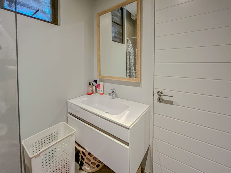 A modern bathroom featuring a white vanity cabinet with an integrated basin, mixer tap, and a simple wooden-framed mirror.