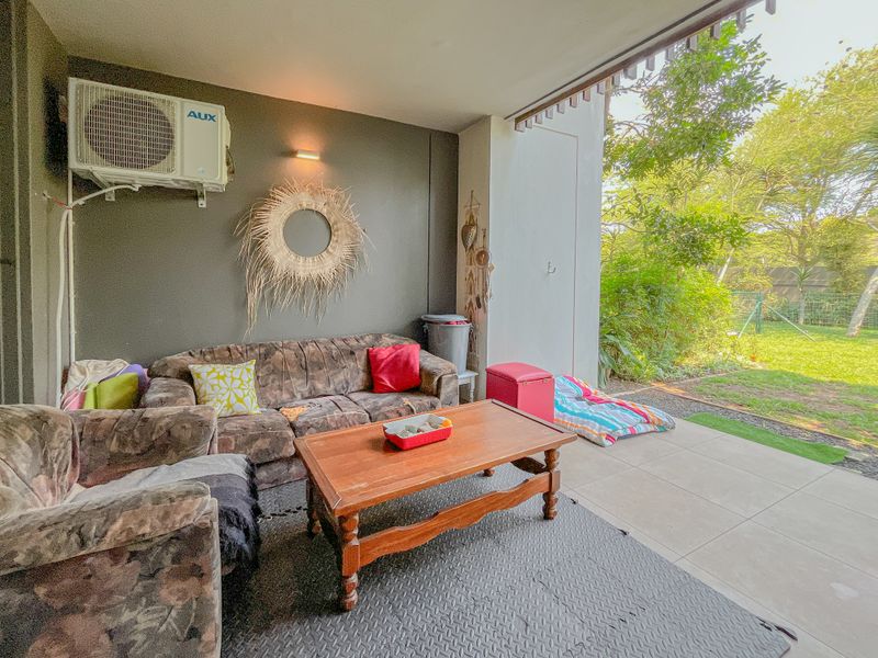 A covered patio area featuring tiled flooring and a wall-mounted air conditioning unit, providing direct access to the garden.