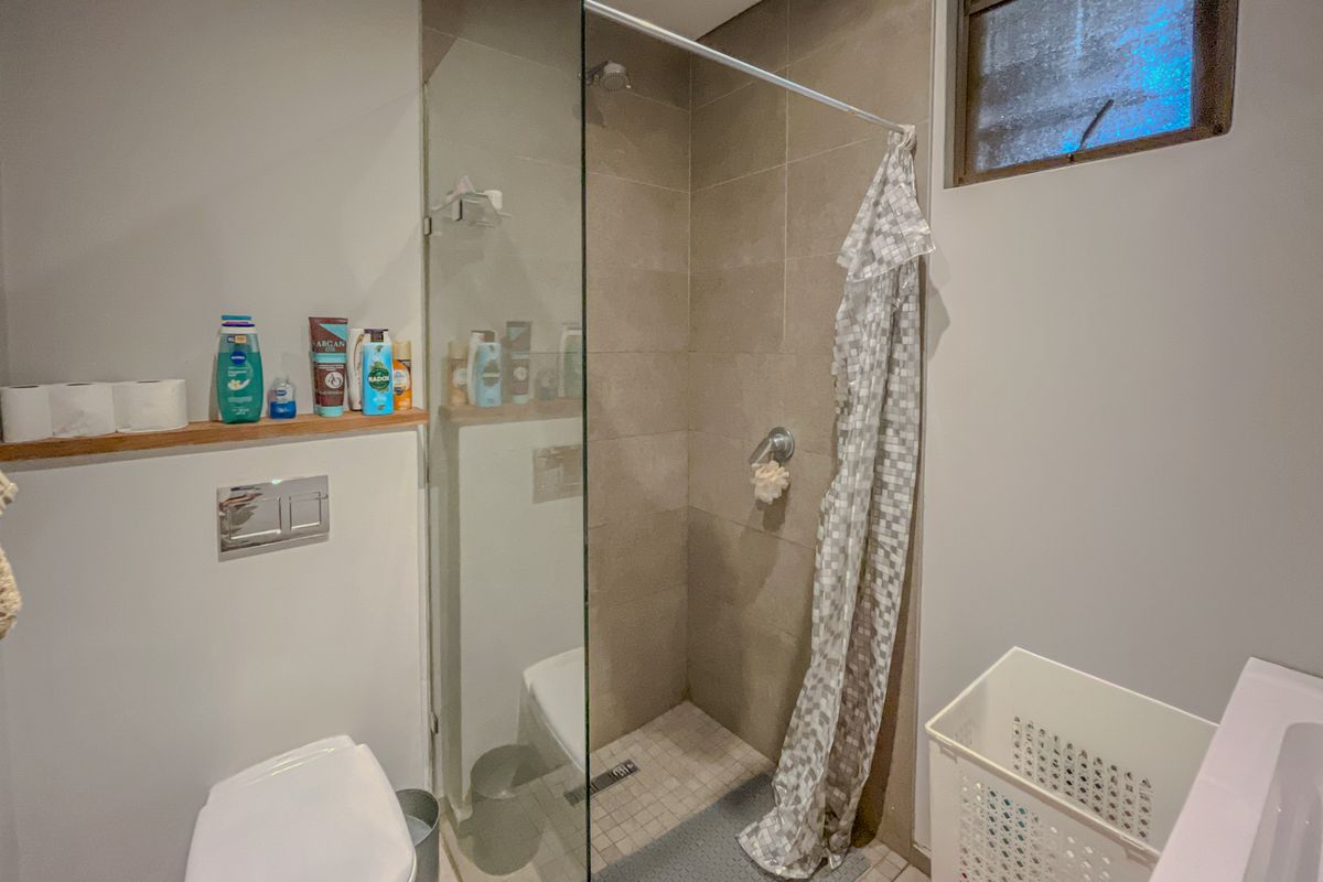 A modern bathroom featuring a walk-in shower with a glass screen, wall-mounted toilet, and neutral tiled finishes.