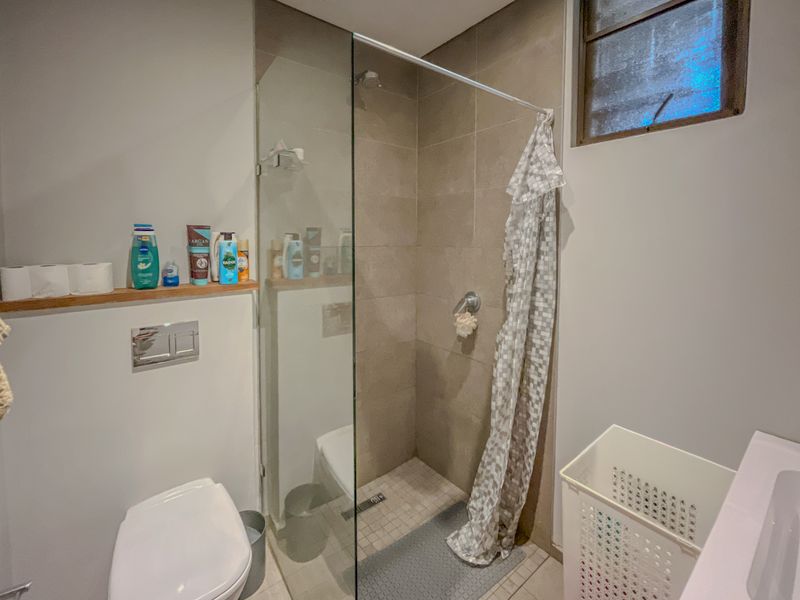 A modern bathroom featuring a walk-in shower with a glass screen, wall-mounted toilet, and neutral tiled finishes.