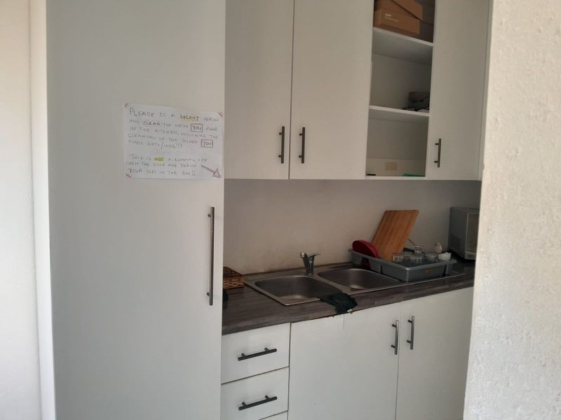 A compact scullery area featuring white built-in cabinetry, a double bowl stainless steel sink, and laminate countertops.